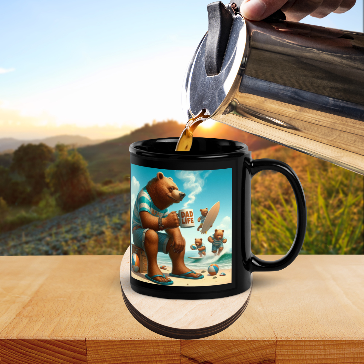 Dad Life Mug collection featuring Boss Beach Bear design, with a single mug on a wooden table outdoors. The background is a mountain landscape and a sunrise. Coffee is being poured into the mug by a silver steel pitcher from the right side. Black, handle right.